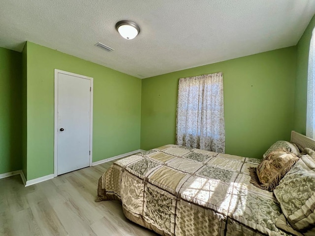 bedroom featuring visible vents, a textured ceiling, baseboards, and wood finished floors
