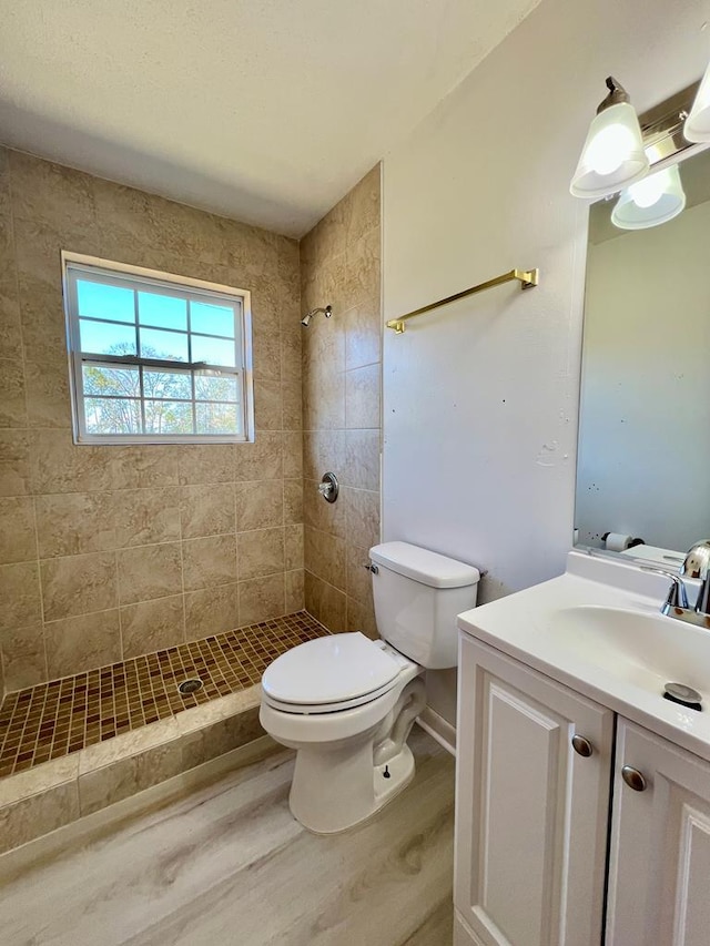 bathroom with toilet, tiled shower, vanity, and wood finished floors