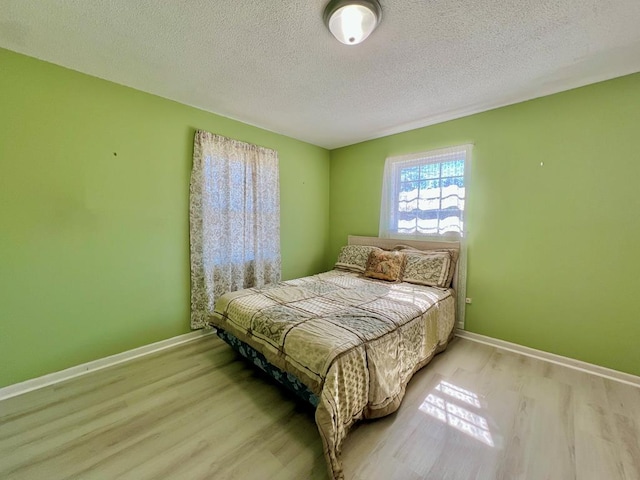 bedroom with wood finished floors, baseboards, and a textured ceiling