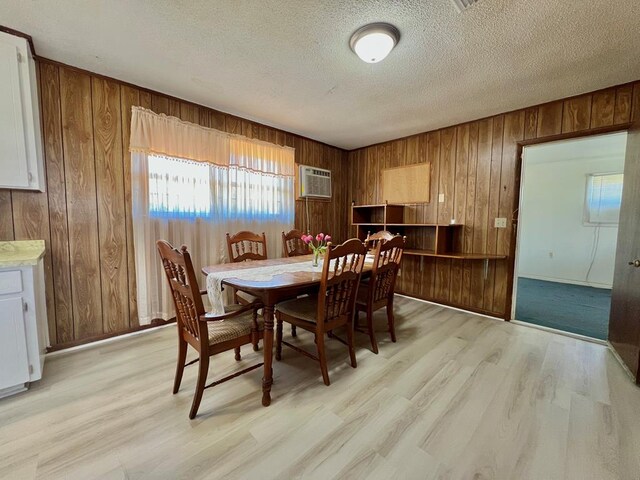 dining space with wooden walls, a wall mounted air conditioner, light wood finished floors, and a textured ceiling