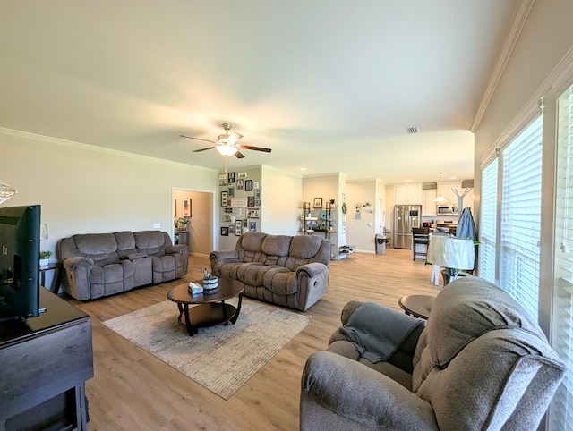 living room featuring ornamental molding, light wood-type flooring, baseboards, visible vents, and a ceiling fan