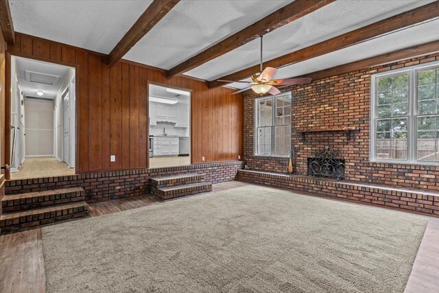 unfurnished living room with ceiling fan, beamed ceiling, wood walls, light hardwood / wood-style floors, and a textured ceiling