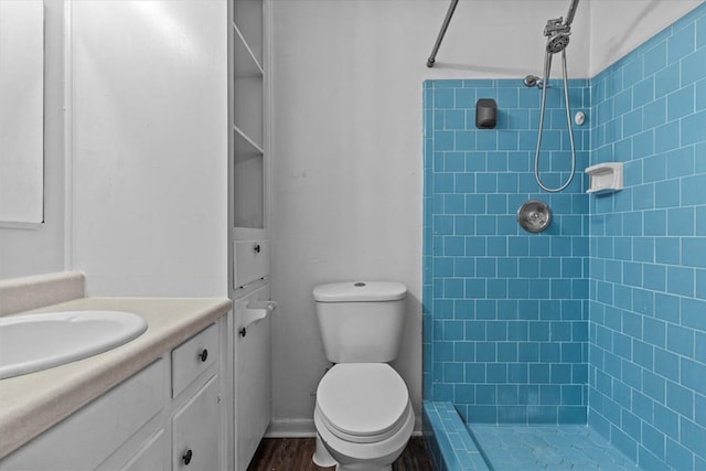 bathroom featuring a tile shower, vanity, toilet, and wood-type flooring