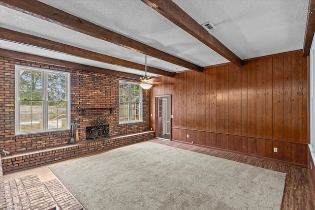 unfurnished living room with a textured ceiling, ceiling fan, wood walls, and hardwood / wood-style flooring