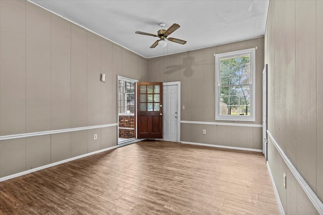 spare room with ceiling fan, wooden walls, and light hardwood / wood-style flooring