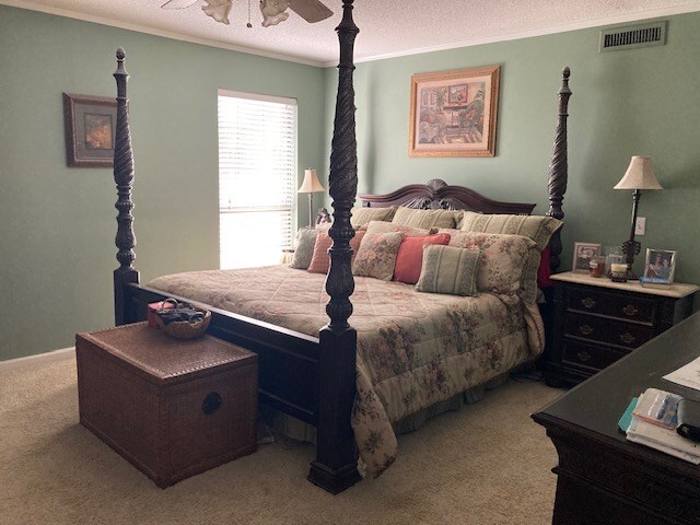 bedroom with a textured ceiling, light colored carpet, ceiling fan, and ornamental molding