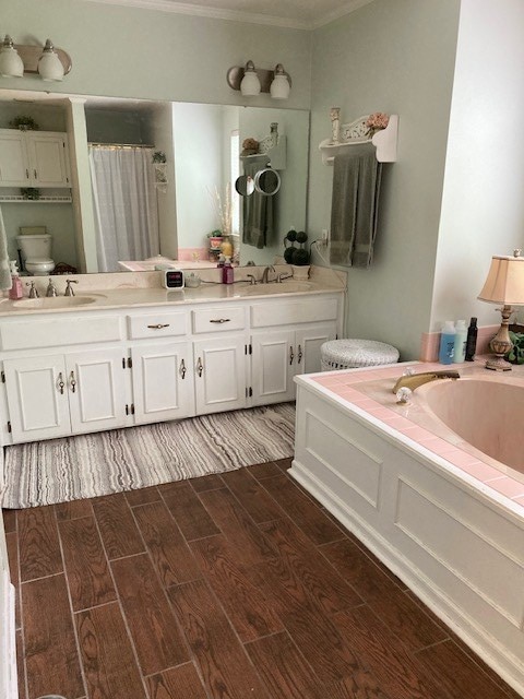 full bathroom featuring a bath, double vanity, a sink, and wood finish floors