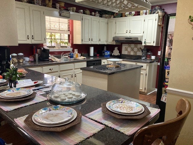 kitchen featuring white cabinets, a sink, dark countertops, and under cabinet range hood