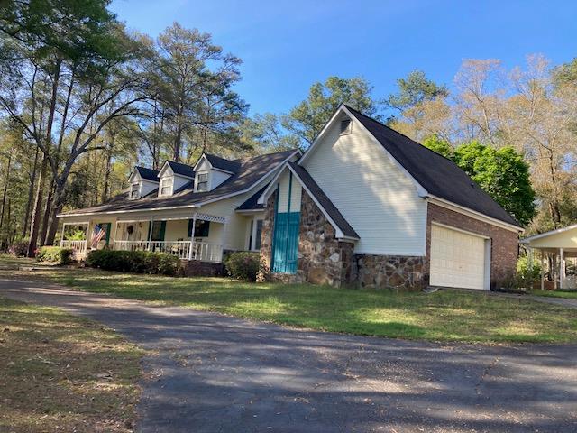 view of property exterior with covered porch, stone siding, a garage, and a yard