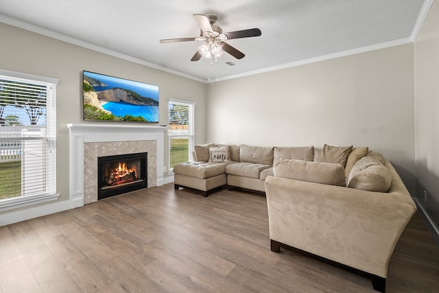 living room featuring a tiled fireplace, a ceiling fan, wood finished floors, and ornamental molding