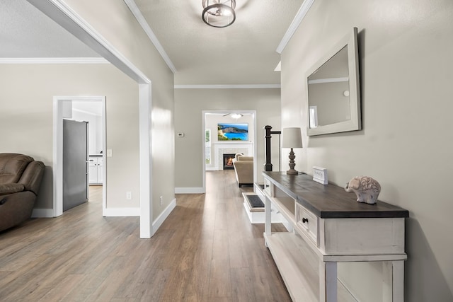 entryway with a warm lit fireplace, baseboards, crown molding, and wood finished floors