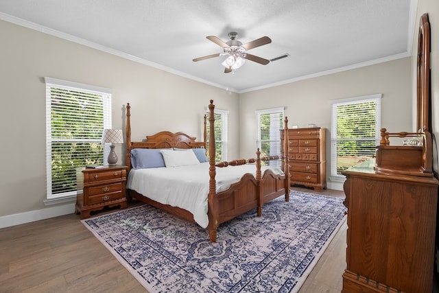 bedroom with multiple windows, wood finished floors, visible vents, and ornamental molding