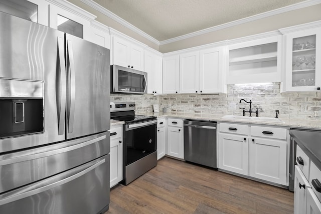 kitchen featuring stainless steel appliances, a sink, tasteful backsplash, white cabinetry, and ornamental molding