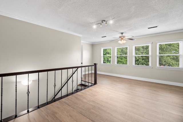 spare room with wood finished floors, a textured ceiling, ceiling fan, ornamental molding, and visible vents