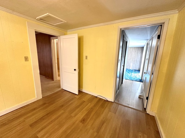 empty room featuring ornamental molding, attic access, baseboards, and wood finished floors