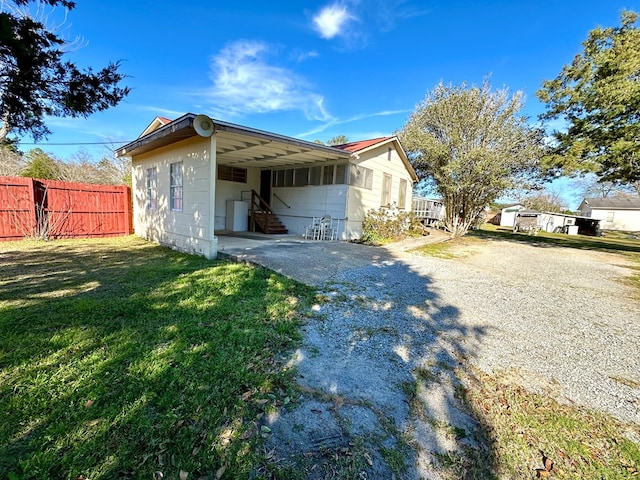 view of property exterior featuring a lawn, driveway, entry steps, fence, and a carport