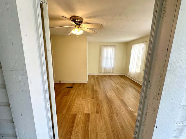 unfurnished room featuring baseboards, visible vents, a ceiling fan, and light wood-style floors