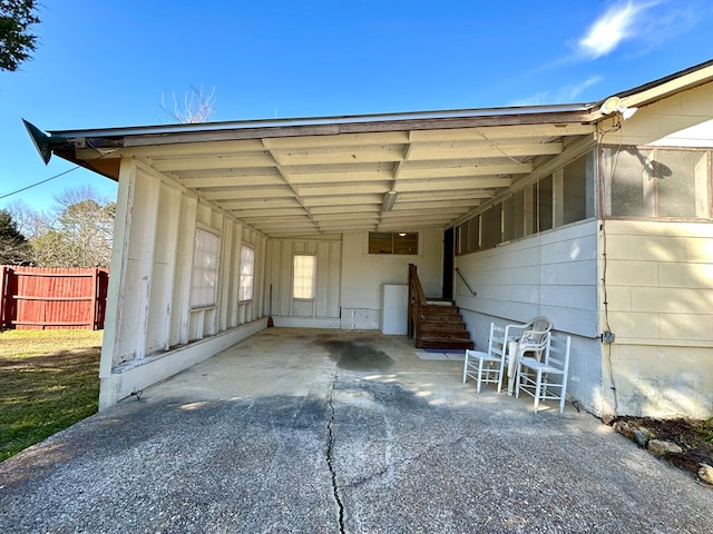 view of parking / parking lot featuring fence, an attached carport, concrete driveway, and entry steps