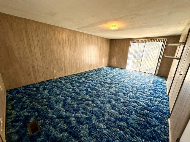 unfurnished room featuring carpet floors, wooden walls, and a textured ceiling