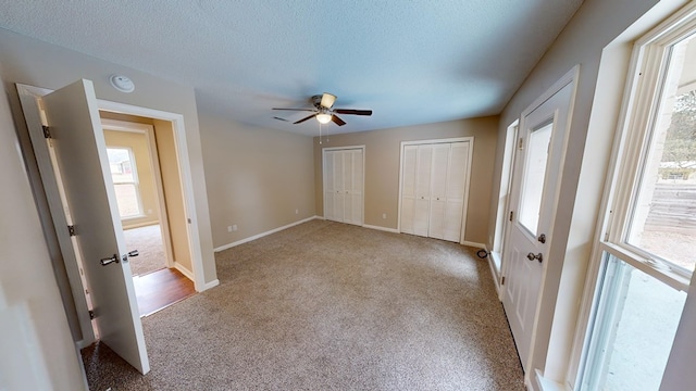 unfurnished bedroom with multiple closets, light carpet, ceiling fan, and a textured ceiling