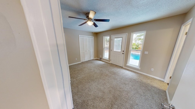 entrance foyer with ceiling fan, a textured ceiling, and light carpet