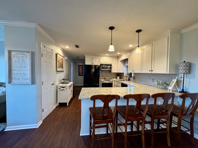 kitchen featuring dark wood-type flooring, stainless steel appliances, pendant lighting, white cabinets, and ornamental molding