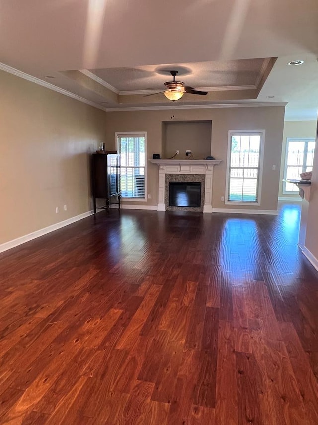 unfurnished living room featuring a raised ceiling, ceiling fan, dark hardwood / wood-style flooring, and crown molding