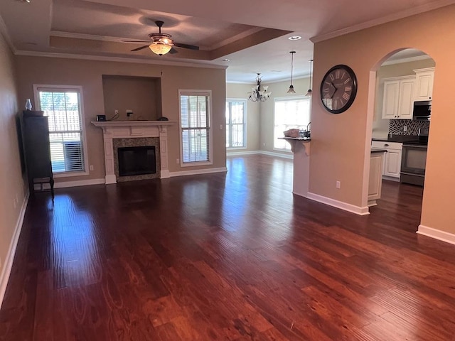 unfurnished living room with a raised ceiling, dark hardwood / wood-style flooring, a healthy amount of sunlight, and ceiling fan with notable chandelier