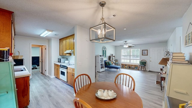 dining area featuring light wood finished floors, a textured ceiling, visible vents, and ceiling fan with notable chandelier