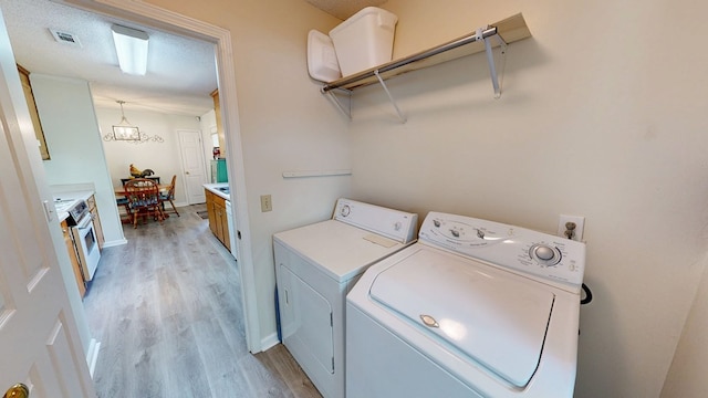 clothes washing area featuring visible vents, washer and dryer, an inviting chandelier, and light wood-style floors