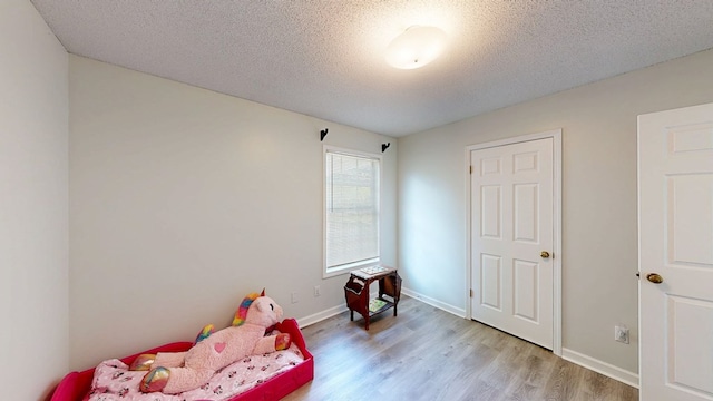 bedroom with a textured ceiling, light wood finished floors, and baseboards