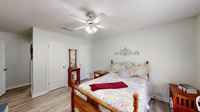 bedroom with light wood finished floors, ceiling fan, visible vents, baseboards, and a textured ceiling