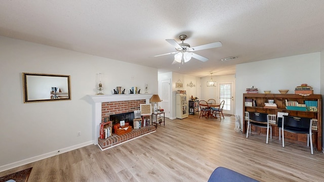living area with visible vents, ceiling fan, baseboards, light wood finished floors, and a brick fireplace
