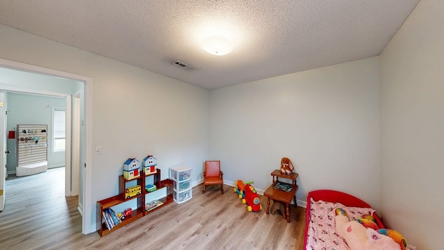 recreation room featuring visible vents, light wood-type flooring, a textured ceiling, and baseboards