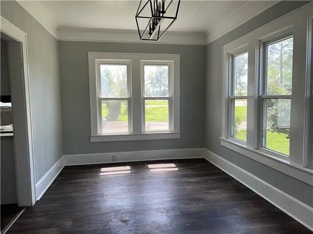 unfurnished dining area with a healthy amount of sunlight, baseboards, ornamental molding, and dark wood-style flooring