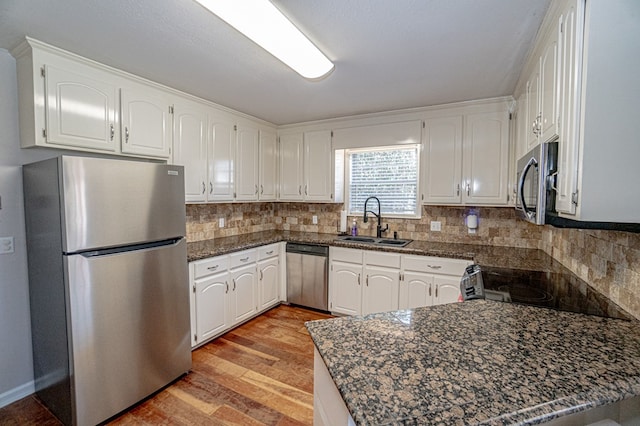 kitchen with dark stone countertops, sink, light hardwood / wood-style flooring, stainless steel appliances, and white cabinets