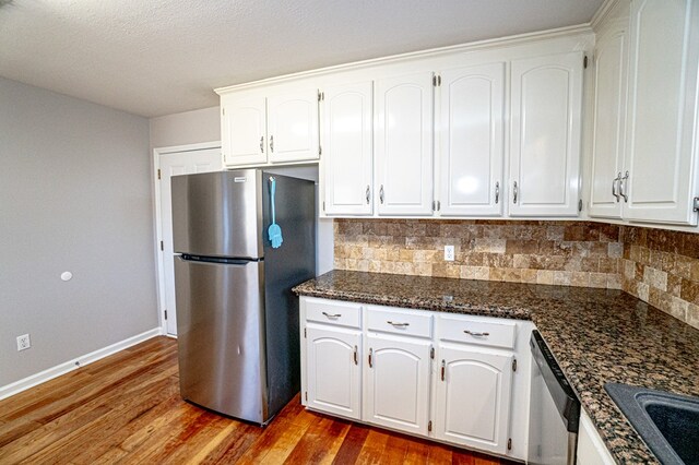 kitchen with white cabinetry, dark hardwood / wood-style flooring, stainless steel appliances, dark stone countertops, and decorative backsplash