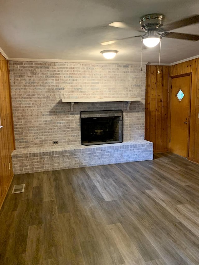 1109 Sumter St, Dothan, AL 36301 - unfurnished living room featuring ceiling fan, a fireplace, brick wall, wood finished floors, and wood walls