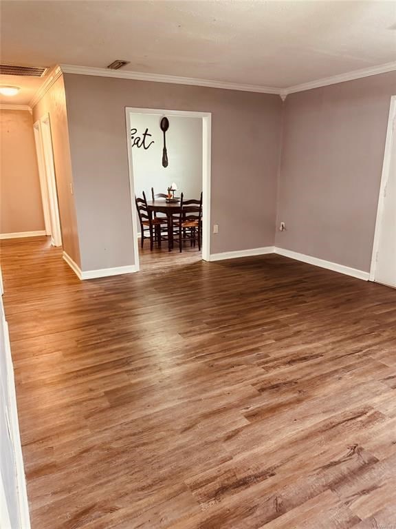 empty room with baseboards, visible vents, crown molding, and wood finished floors