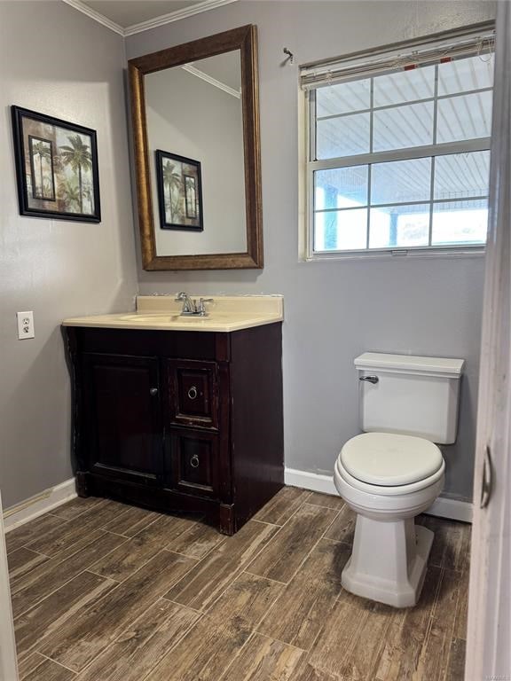 bathroom featuring baseboards, toilet, wood finish floors, and crown molding