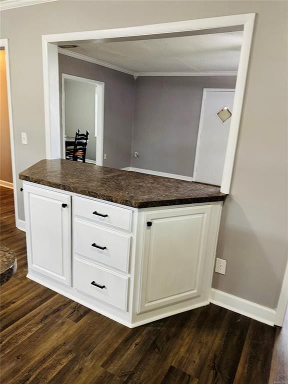 kitchen featuring white cabinets, baseboards, ornamental molding, dark countertops, and dark wood-style floors