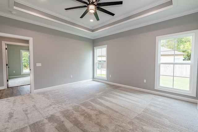 empty room with ceiling fan, light colored carpet, ornamental molding, and a tray ceiling