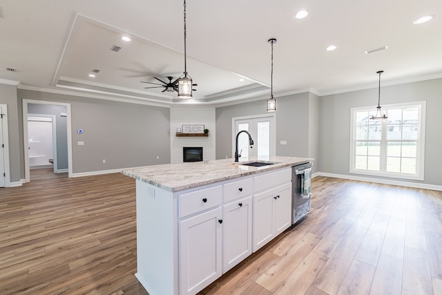 kitchen featuring light stone countertops, light wood-type flooring, a center island with sink, and white cabinetry