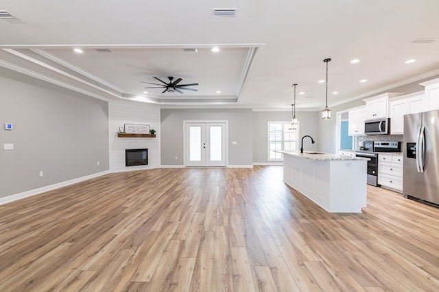 kitchen featuring hanging light fixtures, stainless steel appliances, light hardwood / wood-style flooring, a center island with sink, and white cabinets