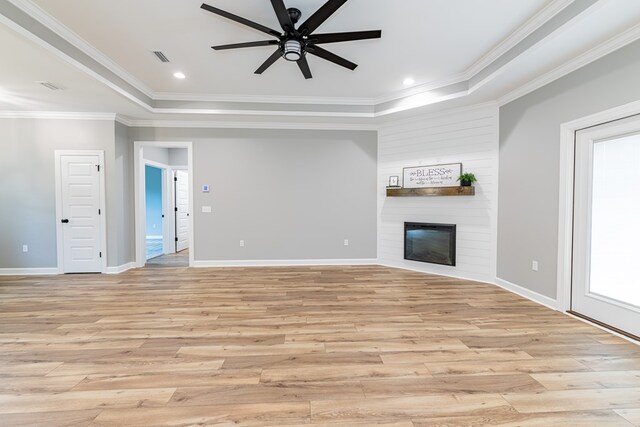 unfurnished living room featuring a raised ceiling, crown molding, light hardwood / wood-style flooring, ceiling fan, and a large fireplace