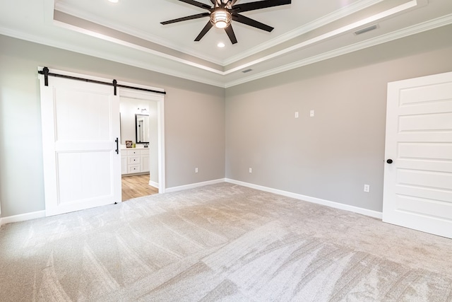 carpeted spare room with a barn door, a tray ceiling, ceiling fan, and crown molding