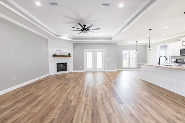 unfurnished living room featuring sink, light hardwood / wood-style flooring, ceiling fan, ornamental molding, and a tray ceiling