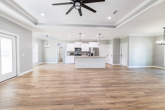 unfurnished living room with a raised ceiling, ceiling fan with notable chandelier, light hardwood / wood-style flooring, and crown molding