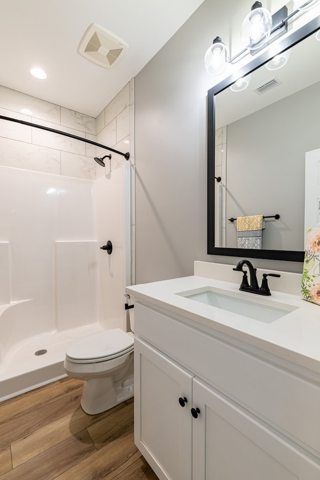 bathroom with wood-type flooring, vanity, a tile shower, and toilet