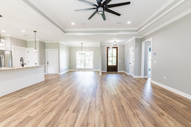 unfurnished living room with ceiling fan with notable chandelier, light wood-type flooring, a raised ceiling, and ornamental molding